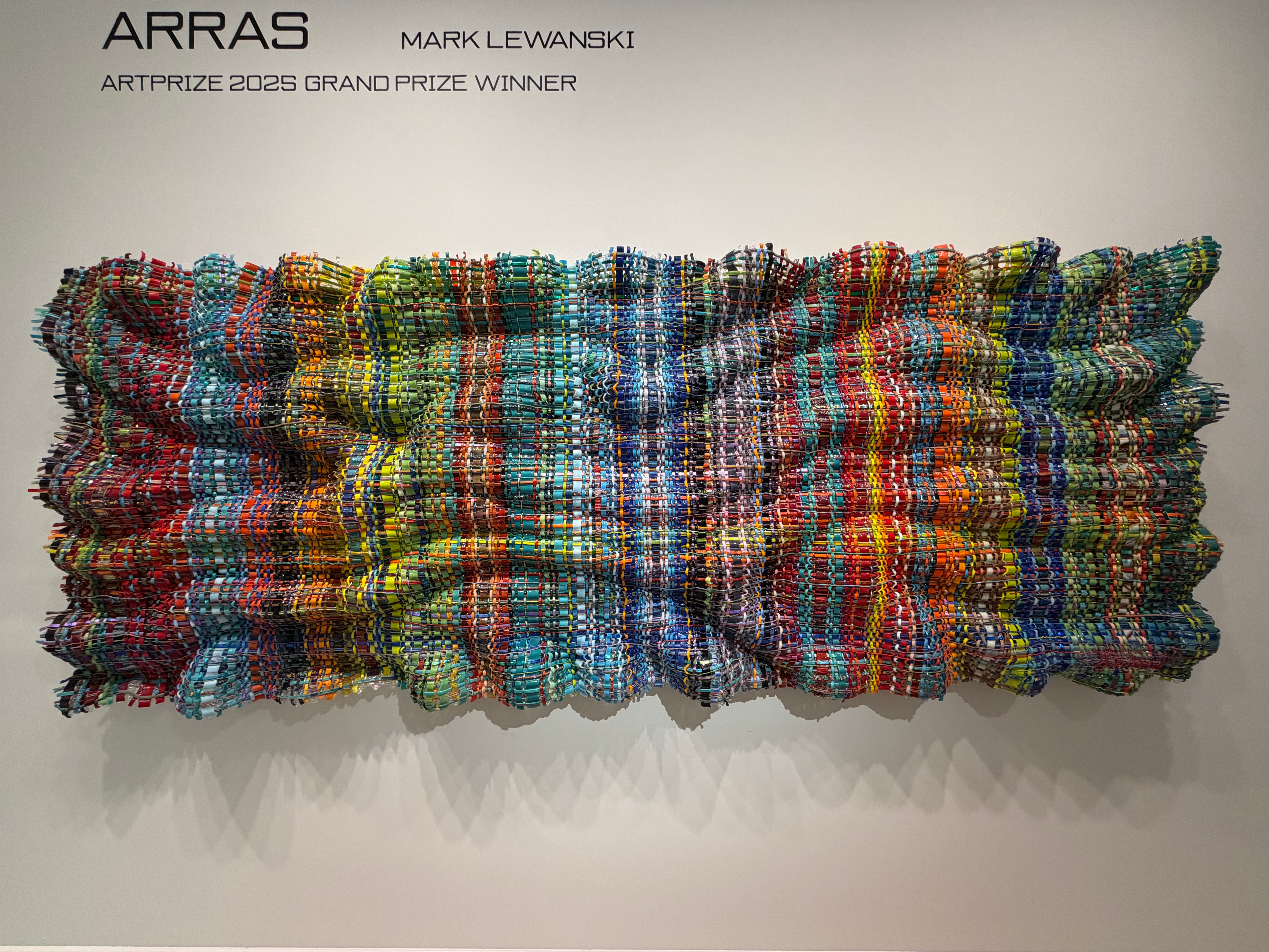 Colorful woven textile with horizontal stripes and textured surface, displayed on a white background.
