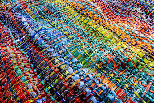 Colorful woven textile with vibrant patterns and textures, featuring various shades of red, blue, green, yellow, and orange.