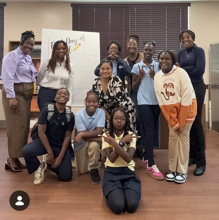 Group of ten people, including children and adults, posing indoors with a whiteboard, smiling, in a classroom or office setting.