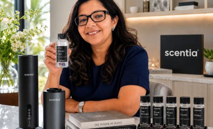 Woman with glasses smiling at a counter with scent products, books, and a black scentia sign in background.