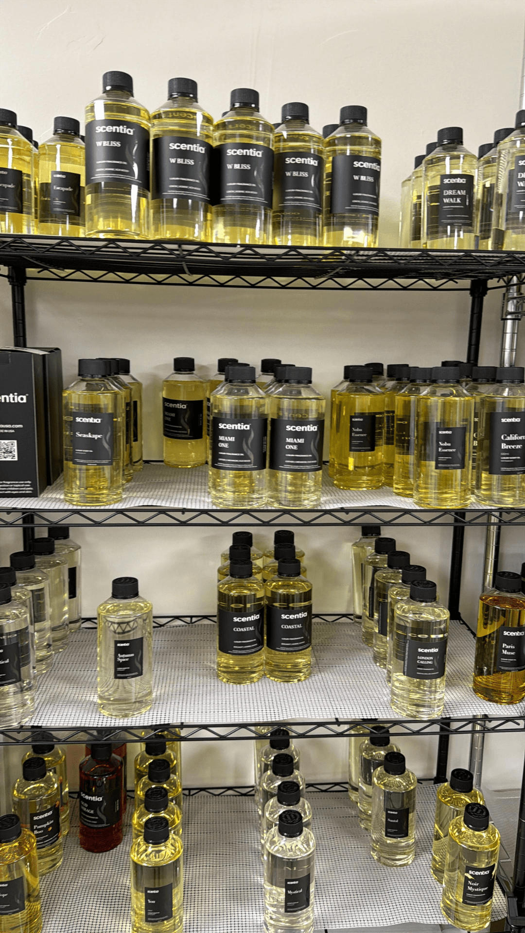 Multiple bottles of yellow liquid on metal shelves against a white wall, arranged in rows and columns.