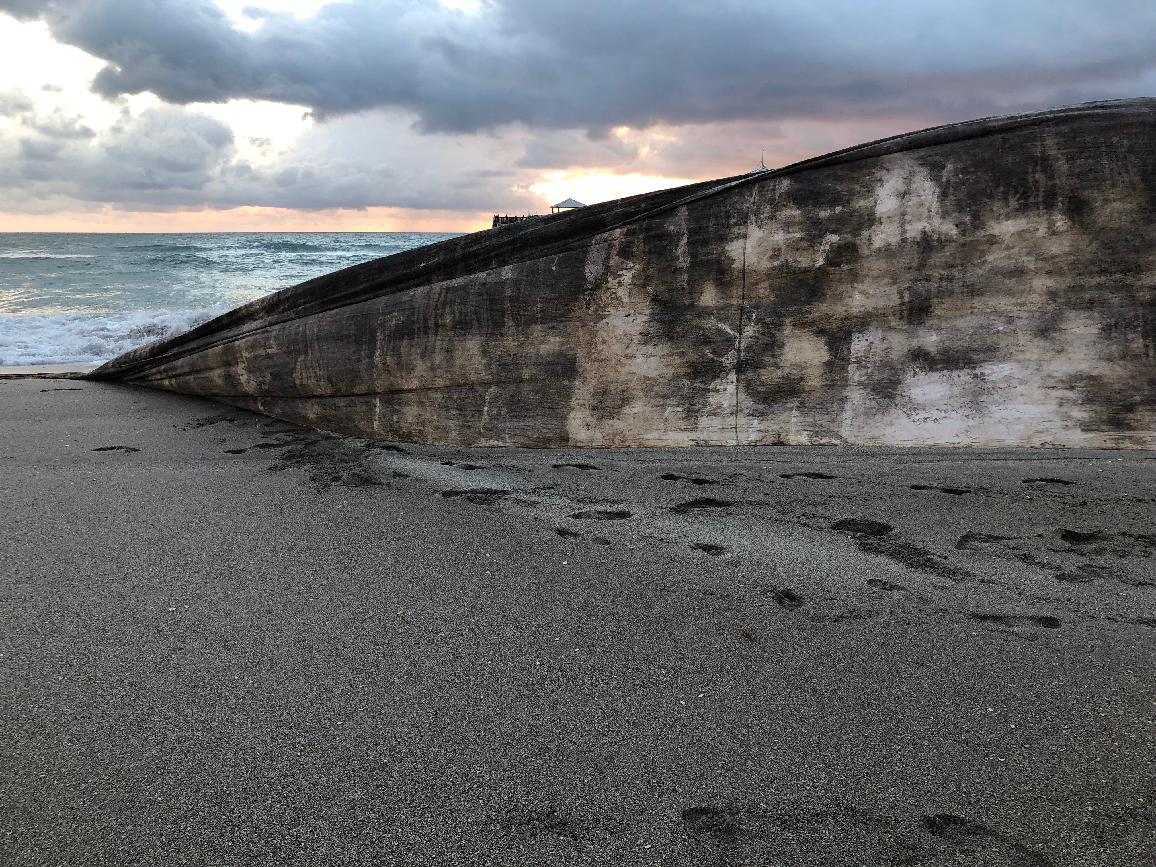 Concrete seawall on sandy beach with footprints, cloudy sky in background.