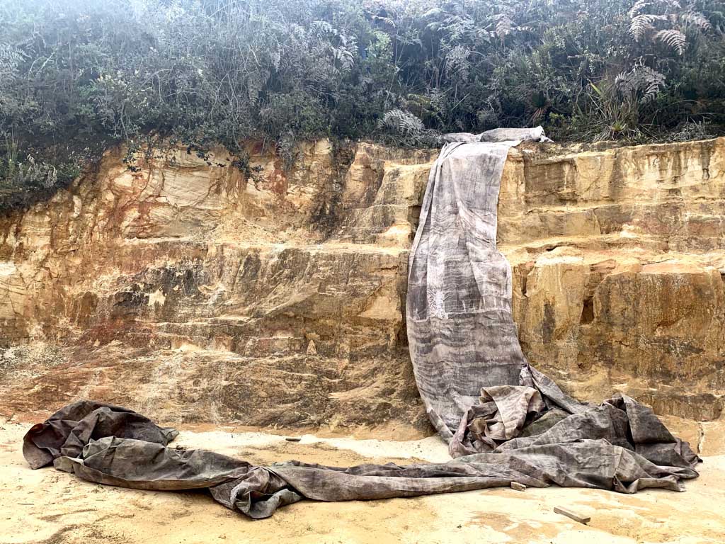 A large fabric or tarp draped over a cliff edge, with part hanging down and pooling on the ground, resembling a waterfall.