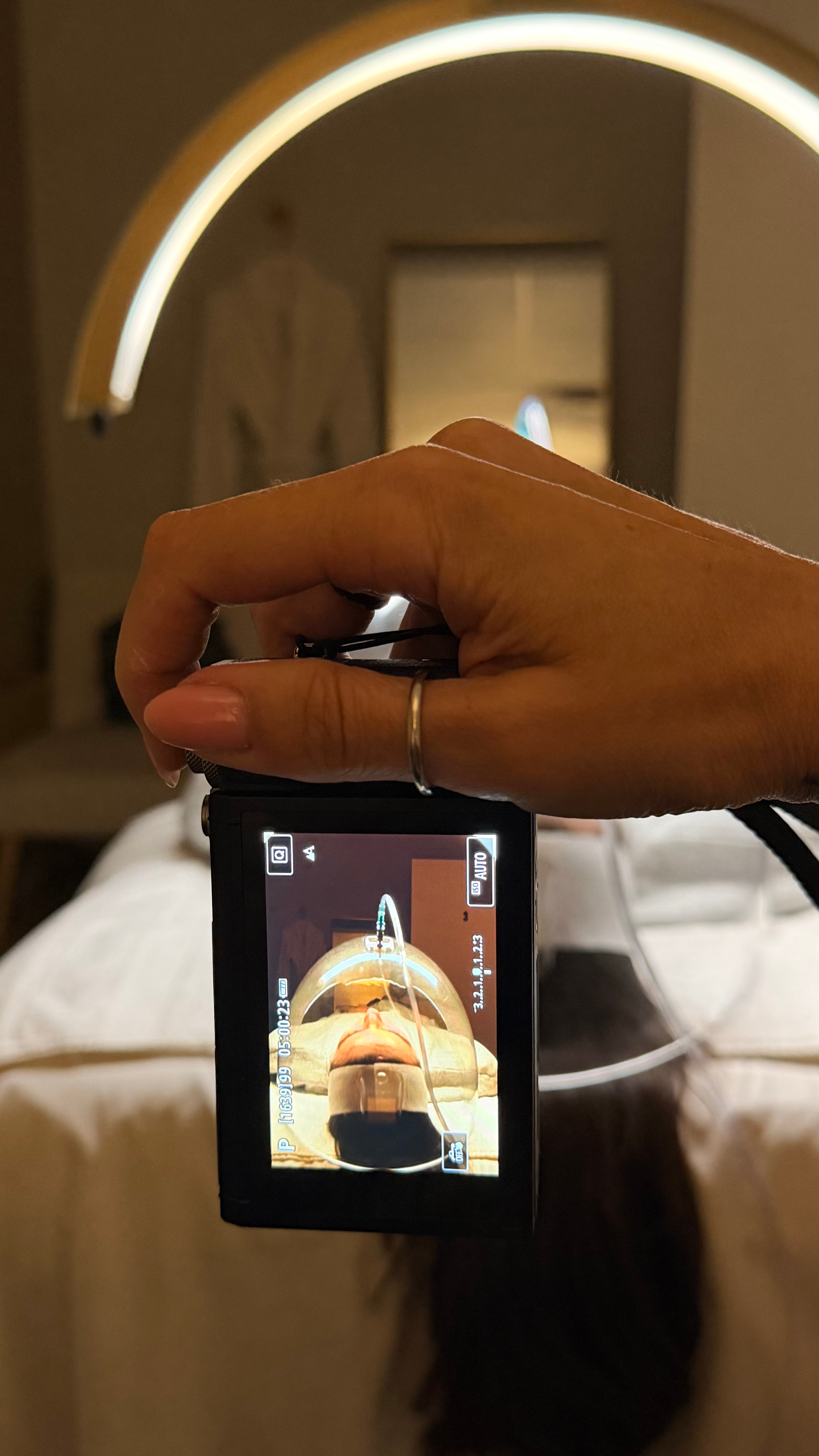 Person holding a camera taking a photo of their reflection in a mirror, with a circular light fixture above.