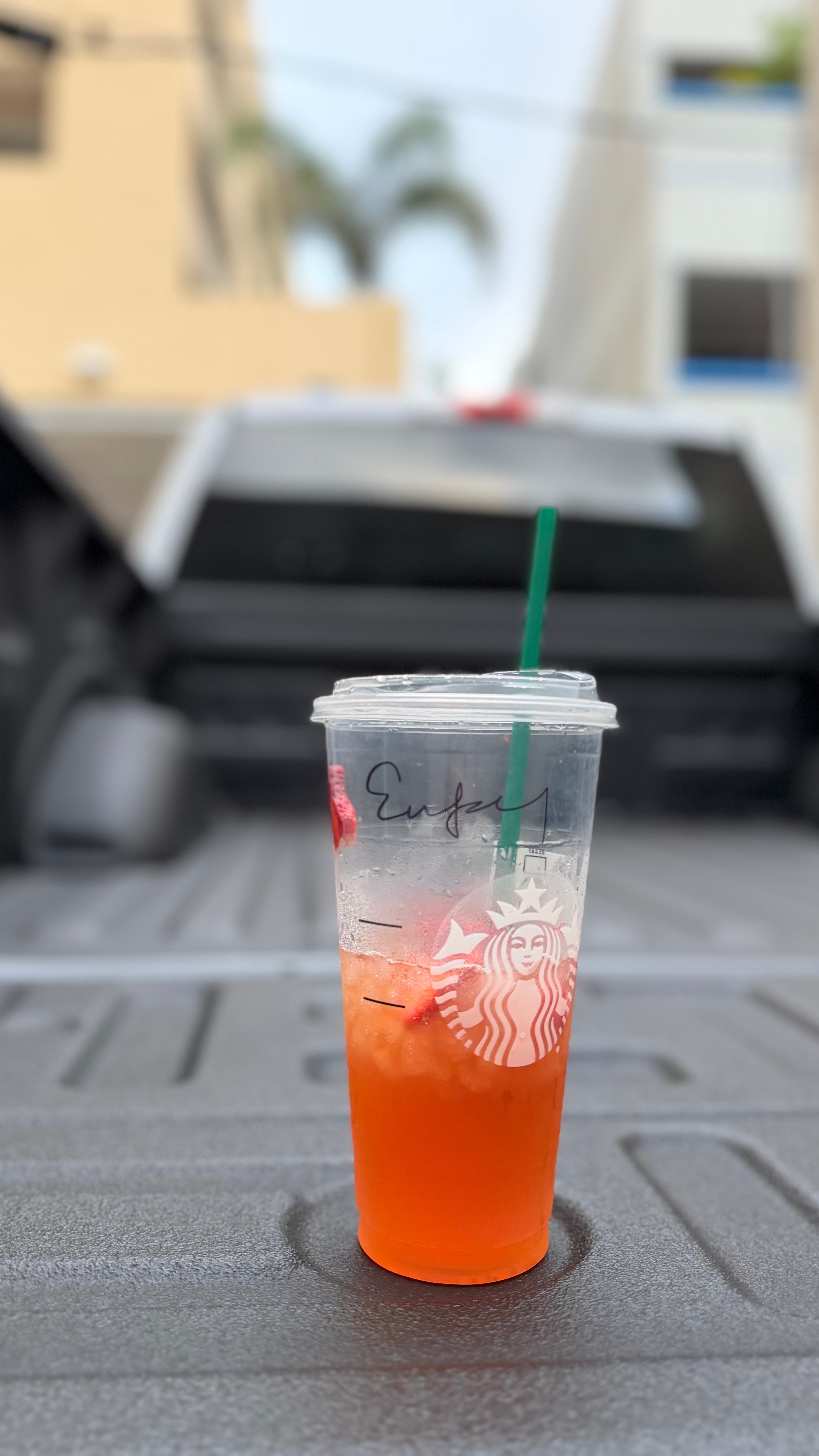 A plastic cup with a green straw, containing a red-orange beverage, placed on a textured surface.