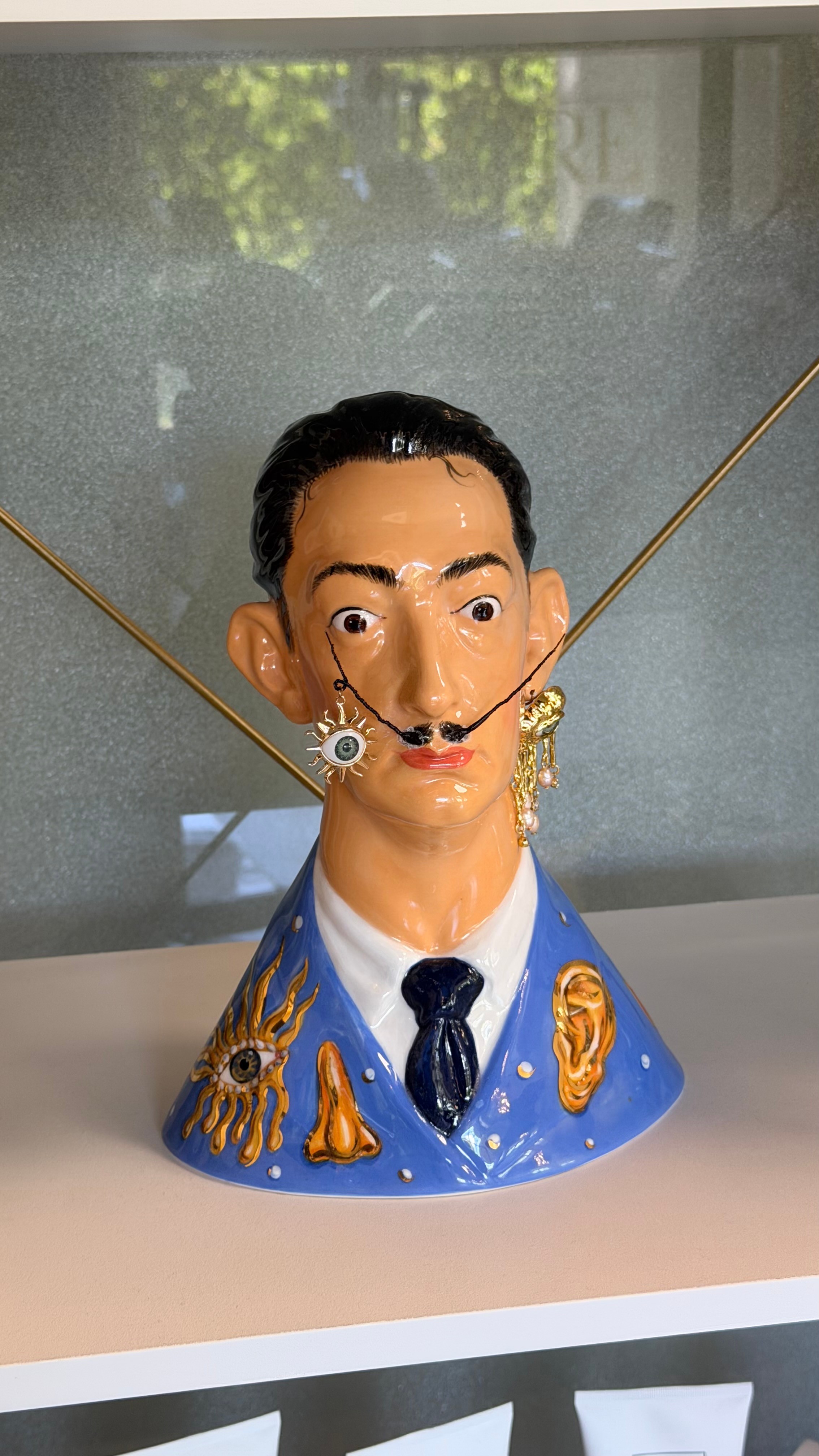 Decorative bust of a man with exaggerated facial features, wearing a blue suit and tie, adorned with gold accents.