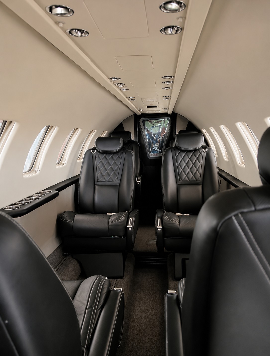 Interior of a private jet with two black leather seats, windows on both sides, and ceiling lights.