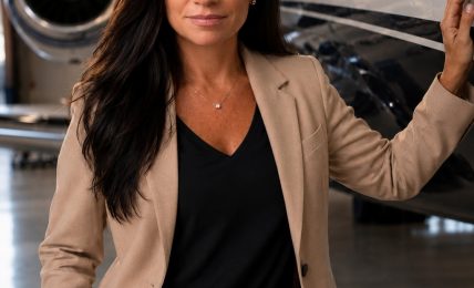 Woman in beige suit standing next to private jet in hangar, looking at camera.